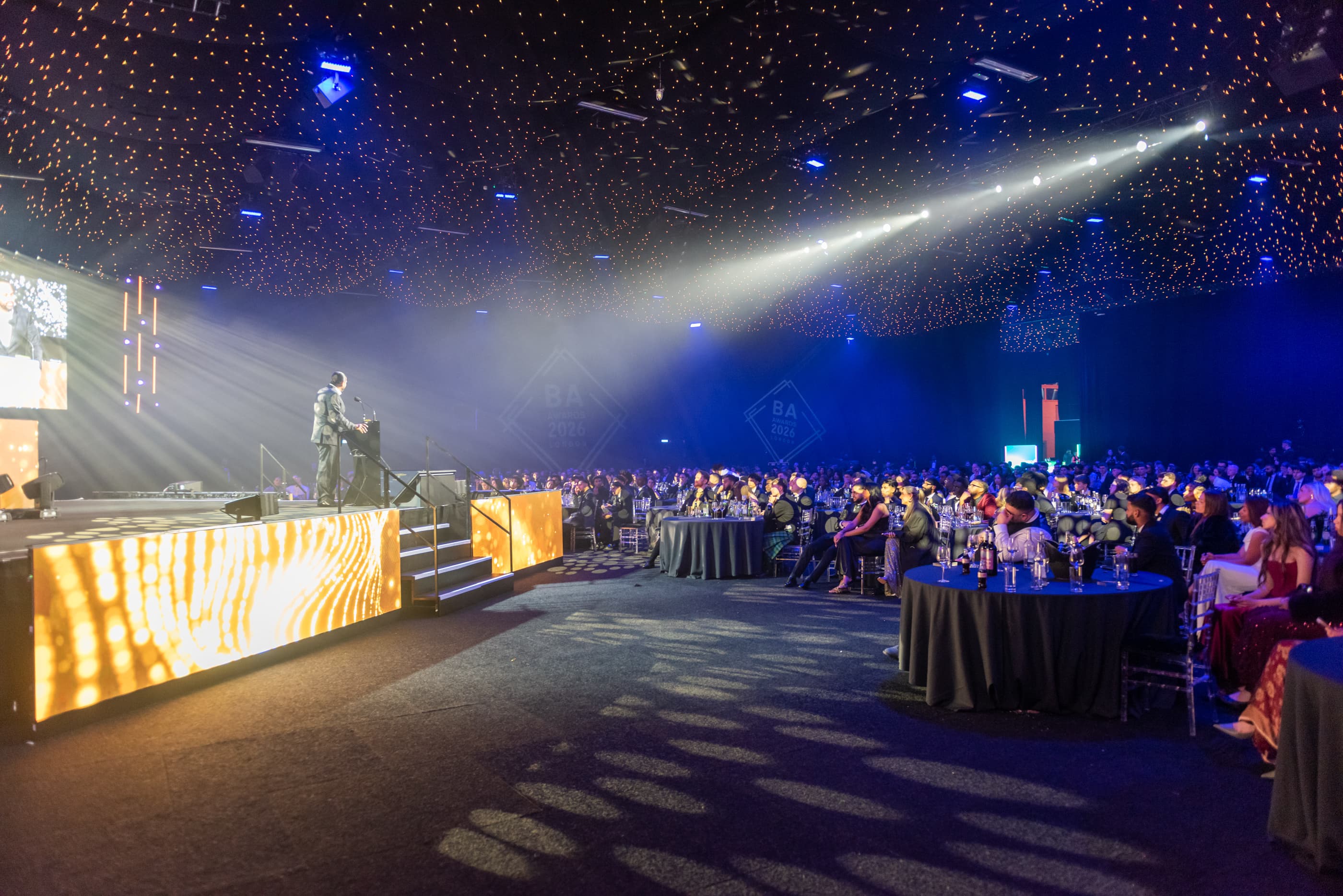 NLS OPTIMA gala event with speaker on stage and large audience